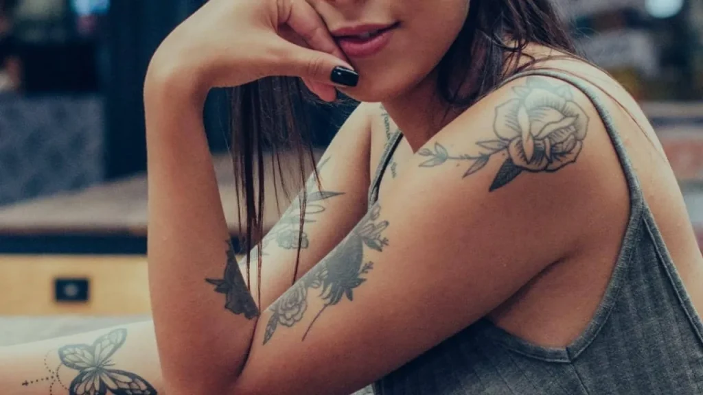 Woman with rose and butterfly tattoos showing how to brighten old tattoos naturally by maintaining skin elasticity and internal health.