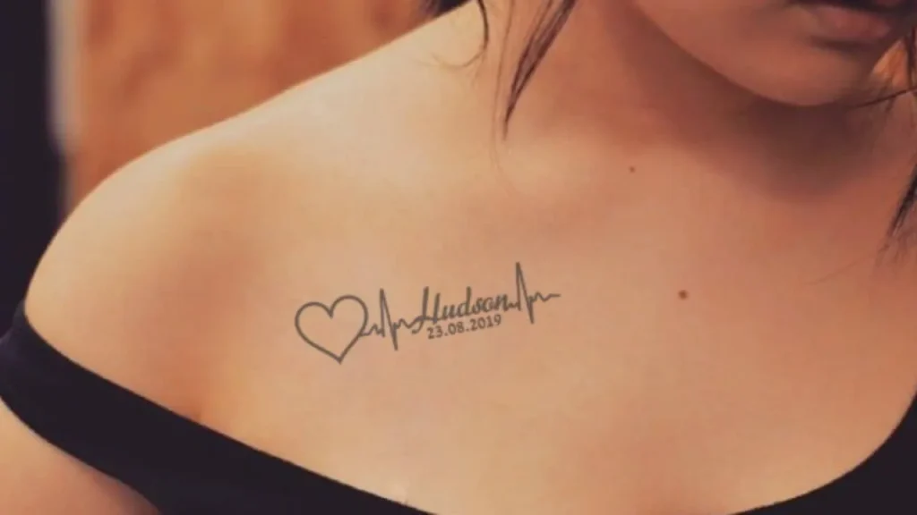 Two women featuring matching fine-line Memorial Handwriting Tattoos on their upper chests with a "Sisters" script and heartbeat design.