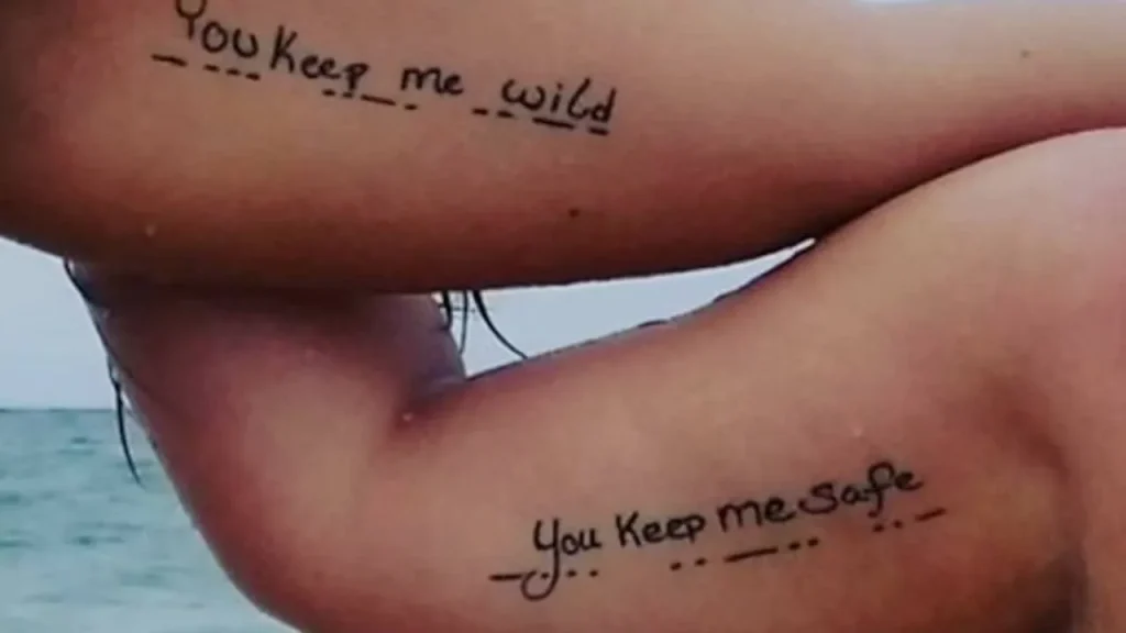 Matching fine-line Memorial Handwriting Tattoos on the inner biceps with Morse code accents.
