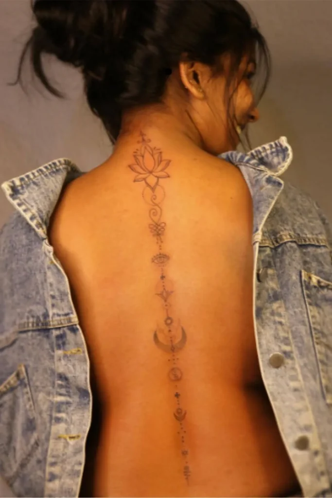 A vertical fine-line Spine Chakra Sacred Geometry Tattoo with a lotus flower and celestial symbols on a woman's back.