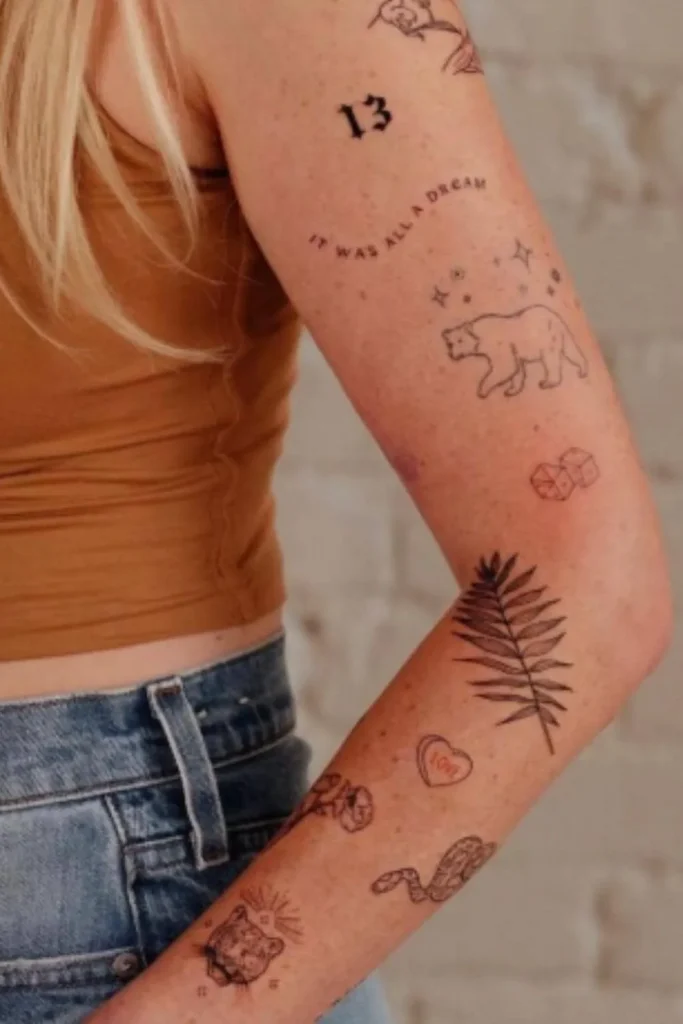 A woman showing a cohesive Y2K sticker sleeve tattoo with fine-line patchwork designs of a bear, palm leaf, and symbols on her arm.