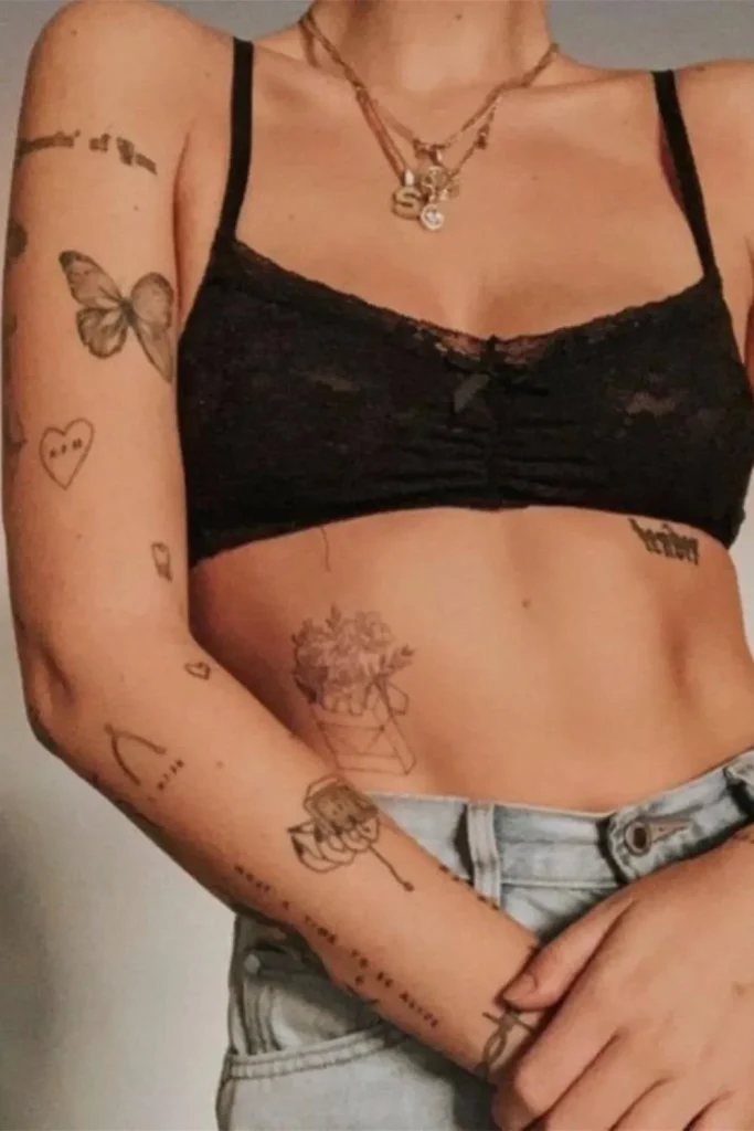 woman showing several small, fine-line tattoos on her arm and torso, illustrating how a Micro Realism Pet Memorial Tattoo fits into a curated collection of tattoos.