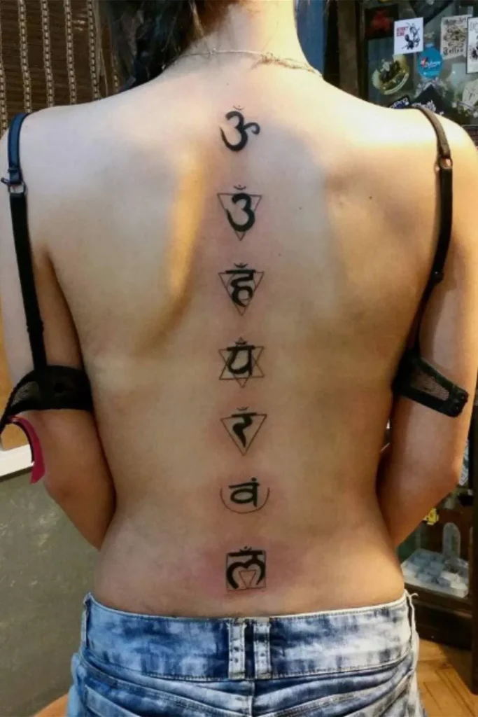 A bold black-ink Spine Chakra Sacred Geometry Tattoo featuring seven symbols in geometric frames aligned vertically on a woman's back.
