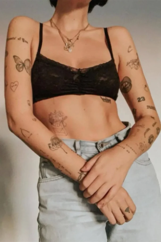 A woman showing several small, fine-line tattoos on her arms and torso, illustrating how a Micro Realism Pet Memorial Tattoo can be part of a meaningful and emotional collection of body art.