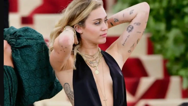 Miley Cyrus is showcasing a cohesive Y2K sticker sleeve tattoo with fine-line patchwork designs on her arms at a red carpet event.