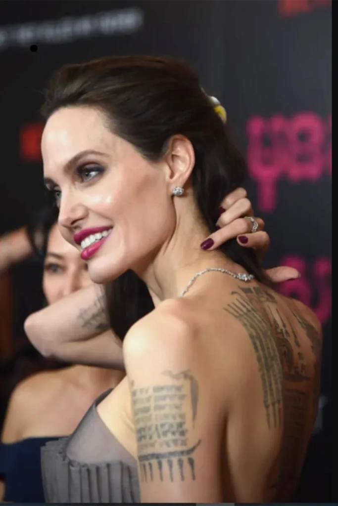 A side profile of Angelina Jolie on the red carpet, displaying her arm coordinates and back tattoos, which connect to the Angelina Jolie Stay Gold Tattoo Meaning.