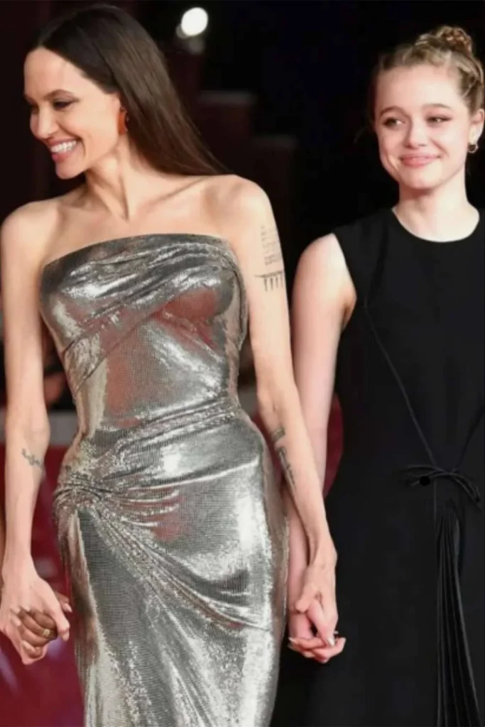 Angelina Jolie holding hands with her daughter Shiloh on a red carpet, displaying her arm tattoos related to the Angelina Jolie Stay Gold Tattoo Meaning.