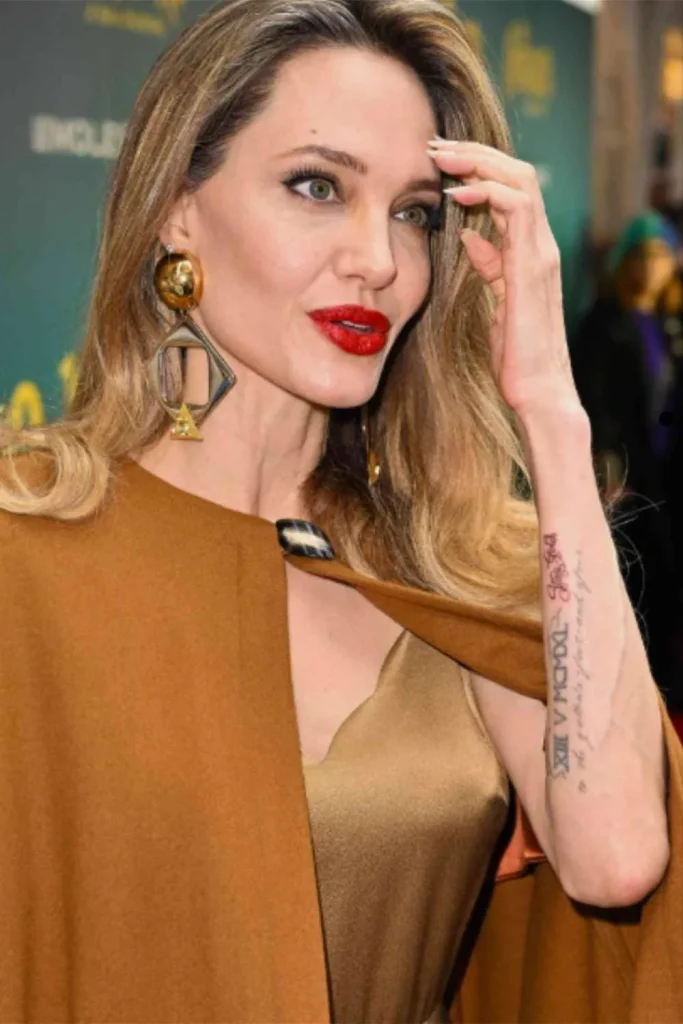 A close-up of Angelina Jolie's forearm showcasing a fine-line script tattoo, highlighting the Angelina Jolie Stay Gold Tattoo Meaning.