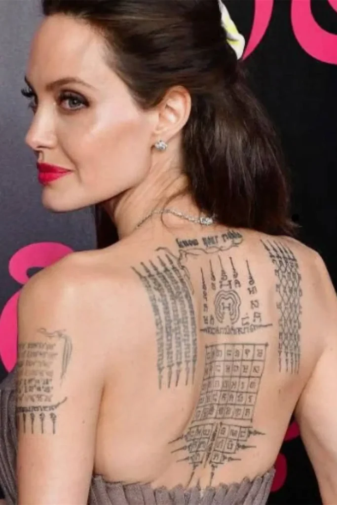 A close-up of Angelina Jolie's back and shoulder tattoos, featuring sacred Thai symbols and script, illustrating the journey toward the Angelina Jolie Stay Gold Tattoo Meaning.