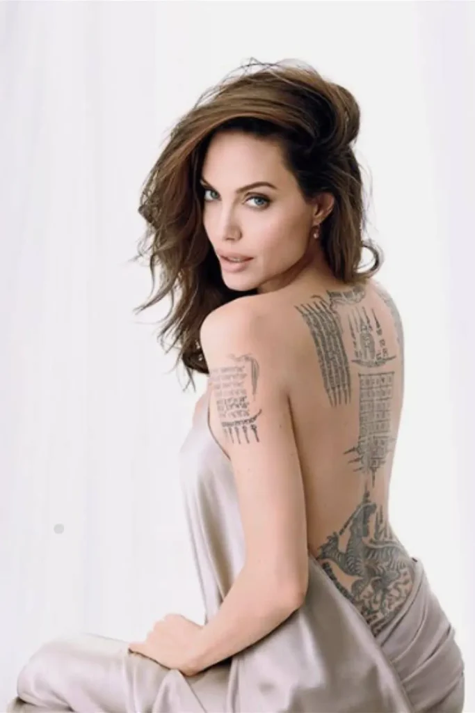 A portrait of Angelina Jolie displaying her full back tattoos, including a Bengal tiger and sacred Thai scripts, providing context for the Angelina Jolie Stay Gold Tattoo Meaning.